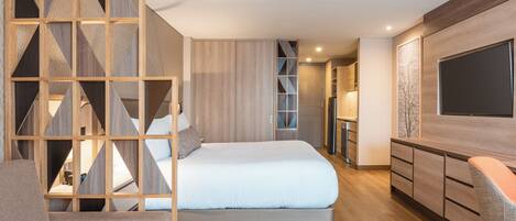 Una habitación de hotel moderna con una cama, un área de descanso, un televisor y un separador de madera.