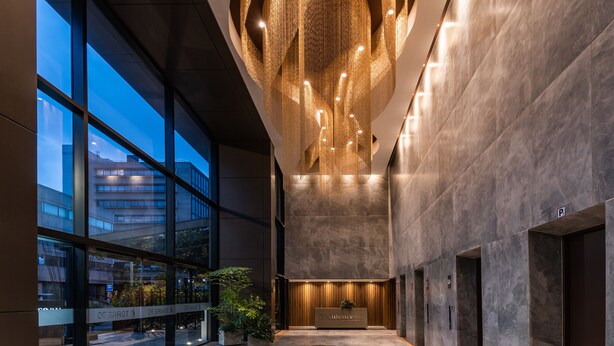 A modern hotel lobby with a high ceiling, large windows, and a central seating area.