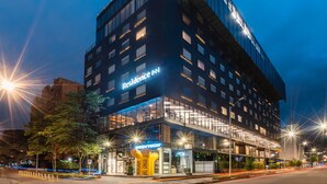 A modern hotel with a glass facade, multiple floors, and illuminated signage.