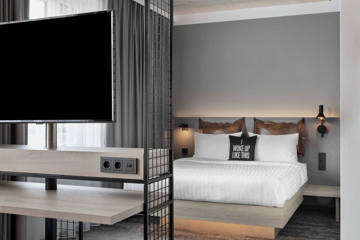 Una habitación de hotel moderna con una cama grande, un televisor y un escritorio con una computadora.