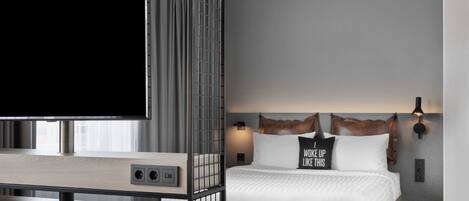 A modern hotel room with a large bed, a TV, and a desk with a computer.