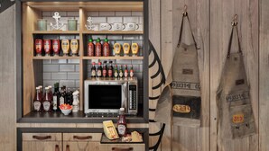 Una cocina con microondas, diferentes condimentos y dos delantales colgados en la pared.