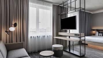 Una habitación de hotel moderna con sofá, una pequeña mesa redonda, televisor sobre un mueble bajo y cama con cabecera.