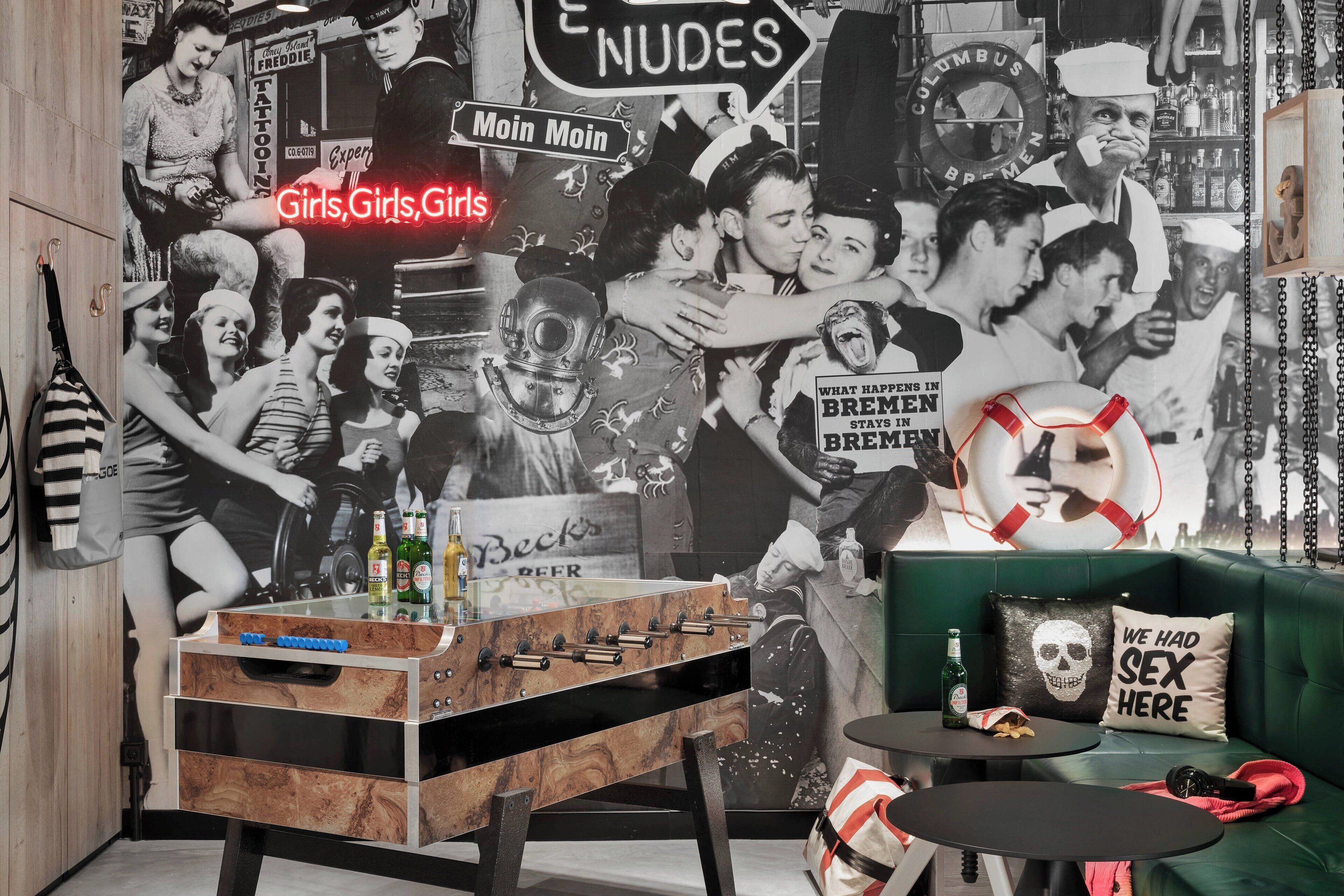 A room with a foosball table, a green sofa, and a wall decorated with vintage posters and a life preserver sign.