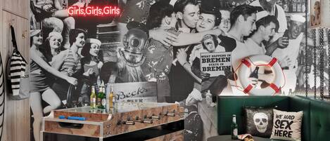 A room with a foosball table, a green sofa, and a wall decorated with vintage posters and a life preserver sign.