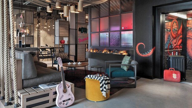 Una sala de estar moderna con un sofá, un reposapiés y una guitarra, una chimenea y un ventanal con vistas a la ciudad.