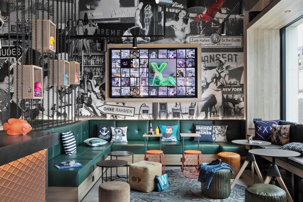 Un área de estar moderna con asientos verdes, una gran pantalla de televisión y varios objetos decorativos.