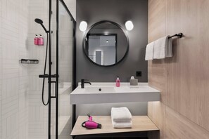 Un baño moderno con cabina de ducha de vidrio, un lavabo blanco con un espejo encima y un mueble de tocador de madera.
