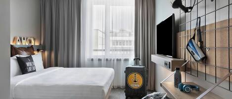 Habitación de hotel con una cama, un escritorio con computadora, una maleta y un televisor montado en la pared.