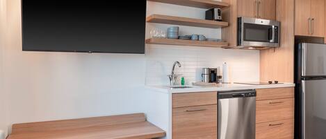 Una cocina moderna con armarios de madera, lavavajillas de acero inoxidable, microondas integrado y televisor de pantalla plana en la pared.