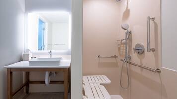 A bathroom with a white sink, wooden vanity, and a shower with a handheld showerhead and grab bars.