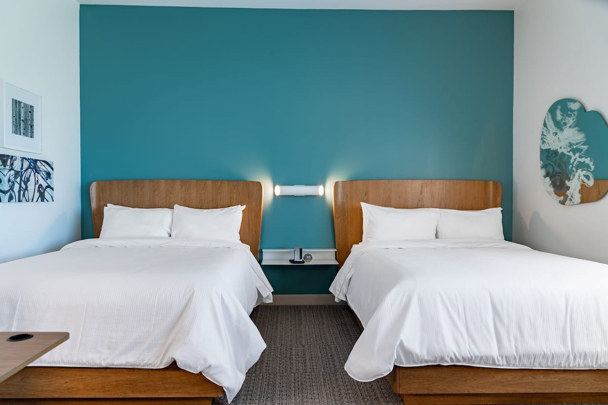 Quarto de hotel com duas camas, paredes cor verde-água e obras de arte nas paredes.