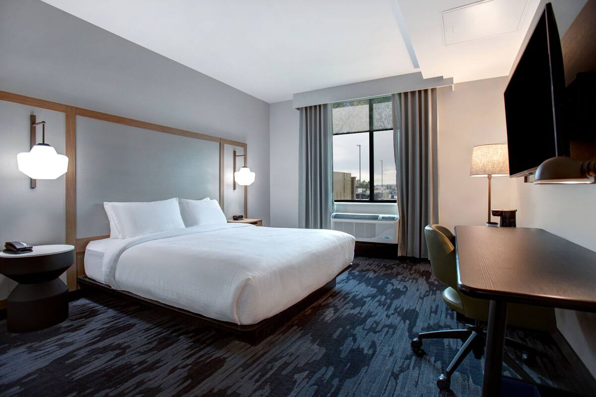 Hotelkamer met een groot bed, een bureau, een stoel, een televisie en een raam met gordijnen.