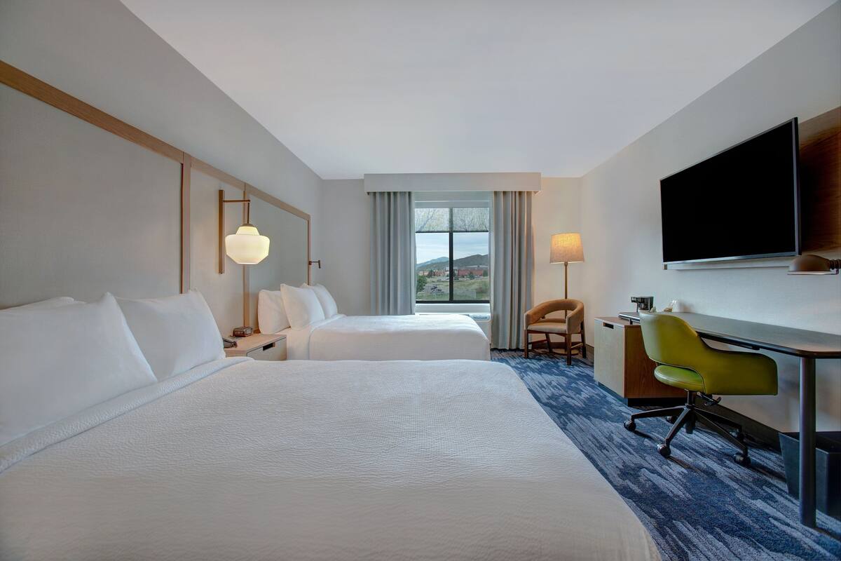 Een hotelkamer met twee bedden, een bureau, een stoel, een televisie en een raam met gordijnen.