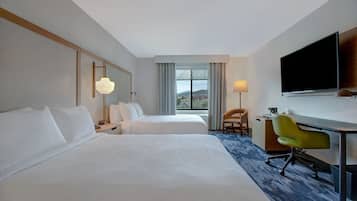 A hotel room with two beds, a desk, a chair, a TV, and a window with curtains.