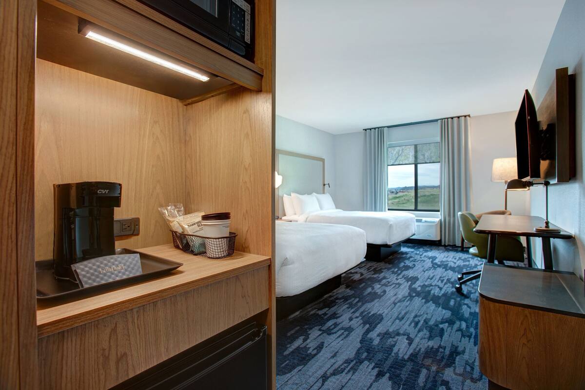 Een hotelkamer met een houten bureau, een koffiezetapparaat, een mandje met toiletartikelen, een bed, een bureau met een lamp en uitzicht op de omgeving.