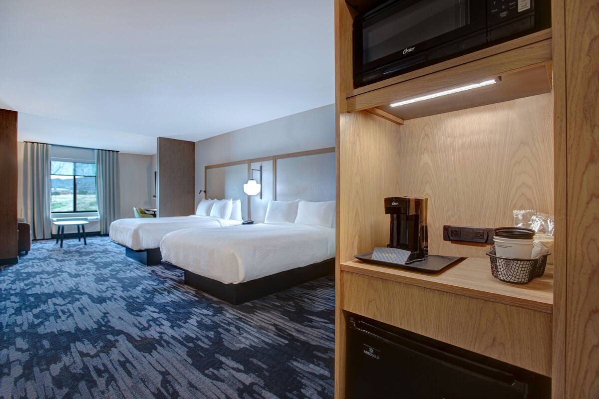 Een hotelkamer met twee bedden, een bureau, een magnetron en een koffiezetapparaat.