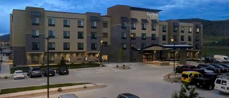 A multi-story hotel with a modern design, featuring a prominent entrance and a parking lot with various vehicles.