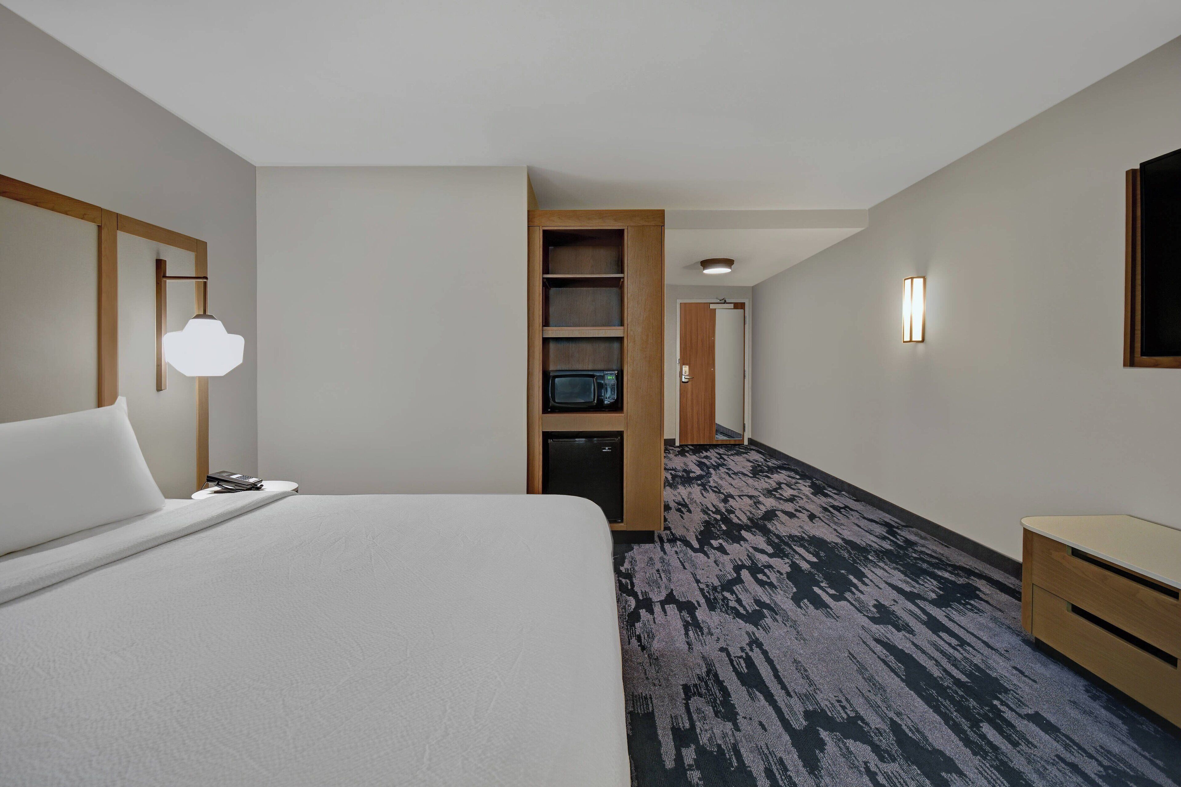 A hotel room with a large bed, a desk, a microwave, and a TV in the corner.