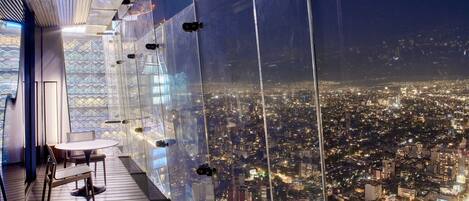 A high-rise room with a panoramic city view, large windows, and a wooden floor.