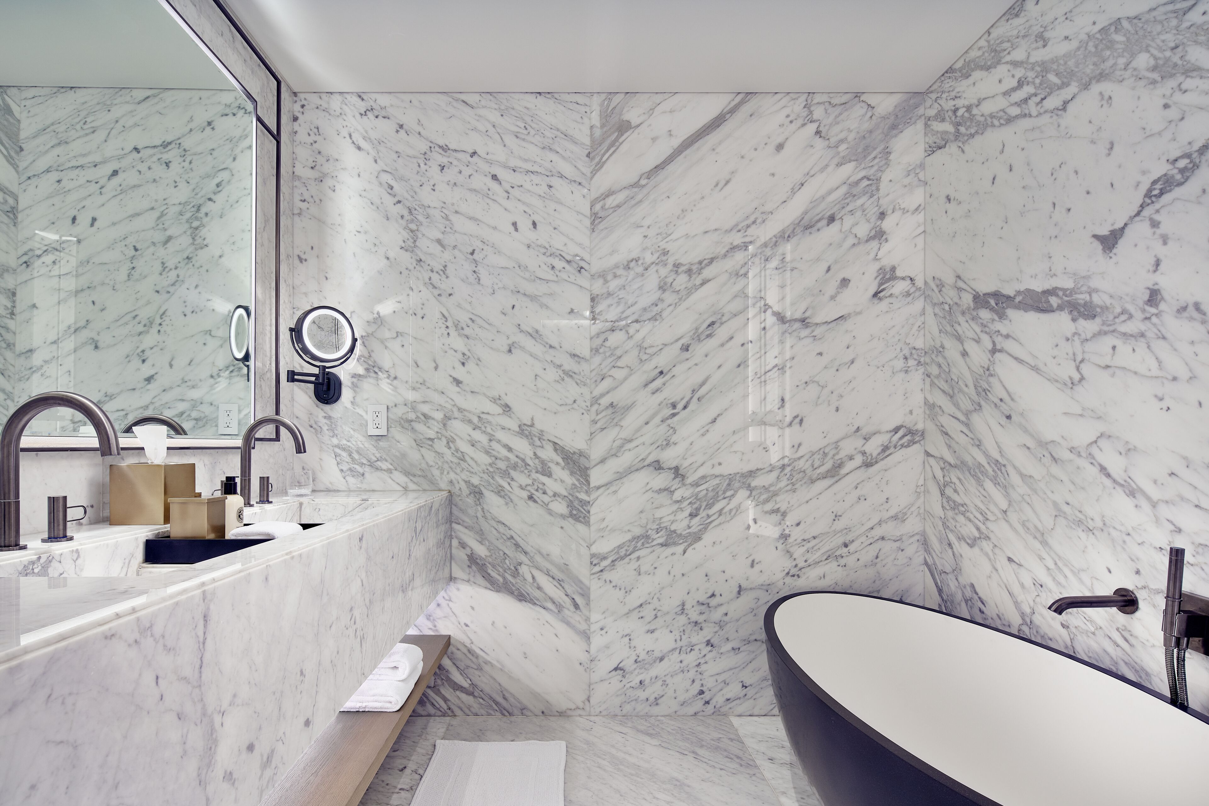 A modern bathroom with a marble backsplash, a freestanding bathtub, and a vanity with a mirror and towel rack.
