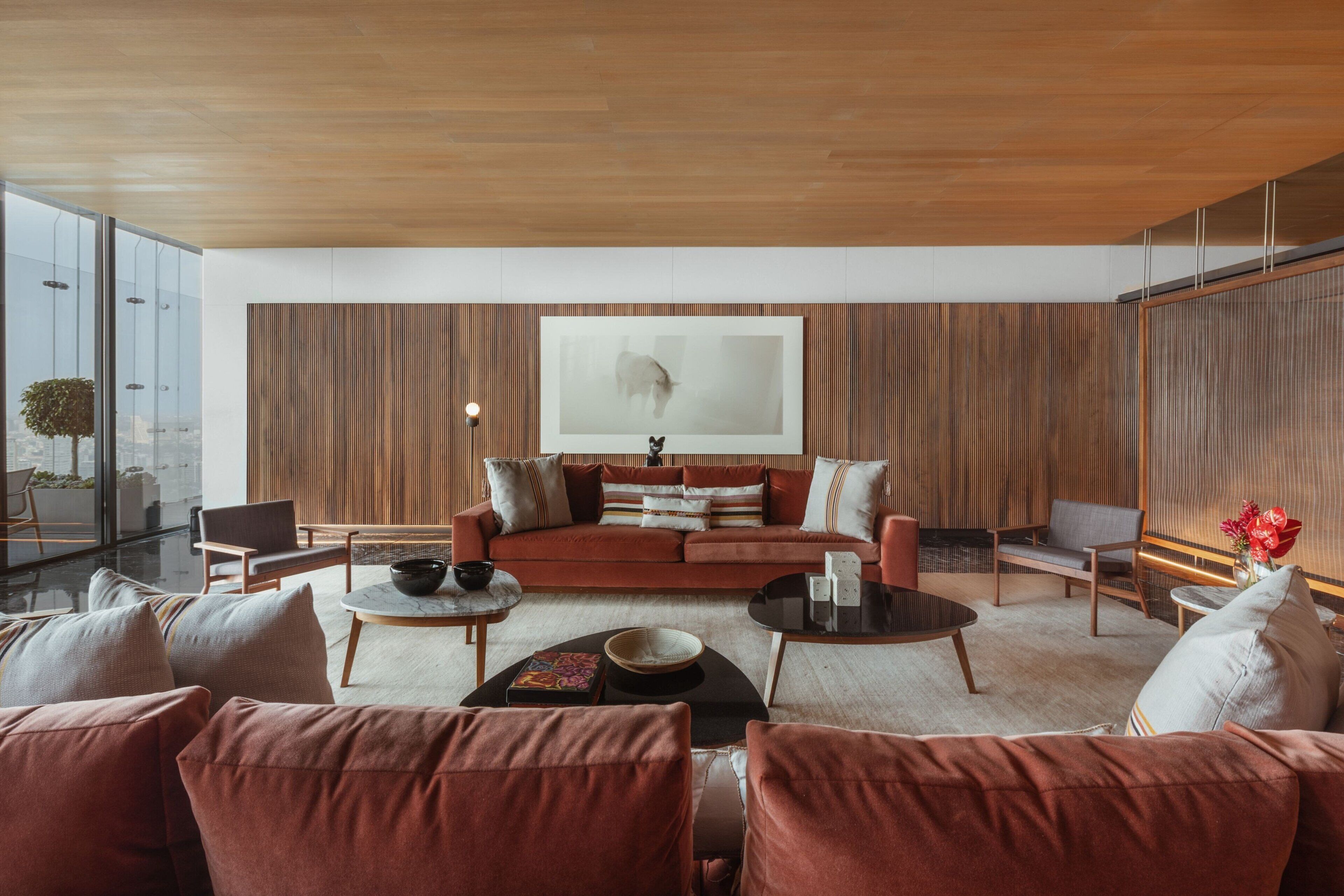A modern living room with a large sofa, two armchairs, and a coffee table. A large abstract painting is on the wall, and there is a window with a view of the city.