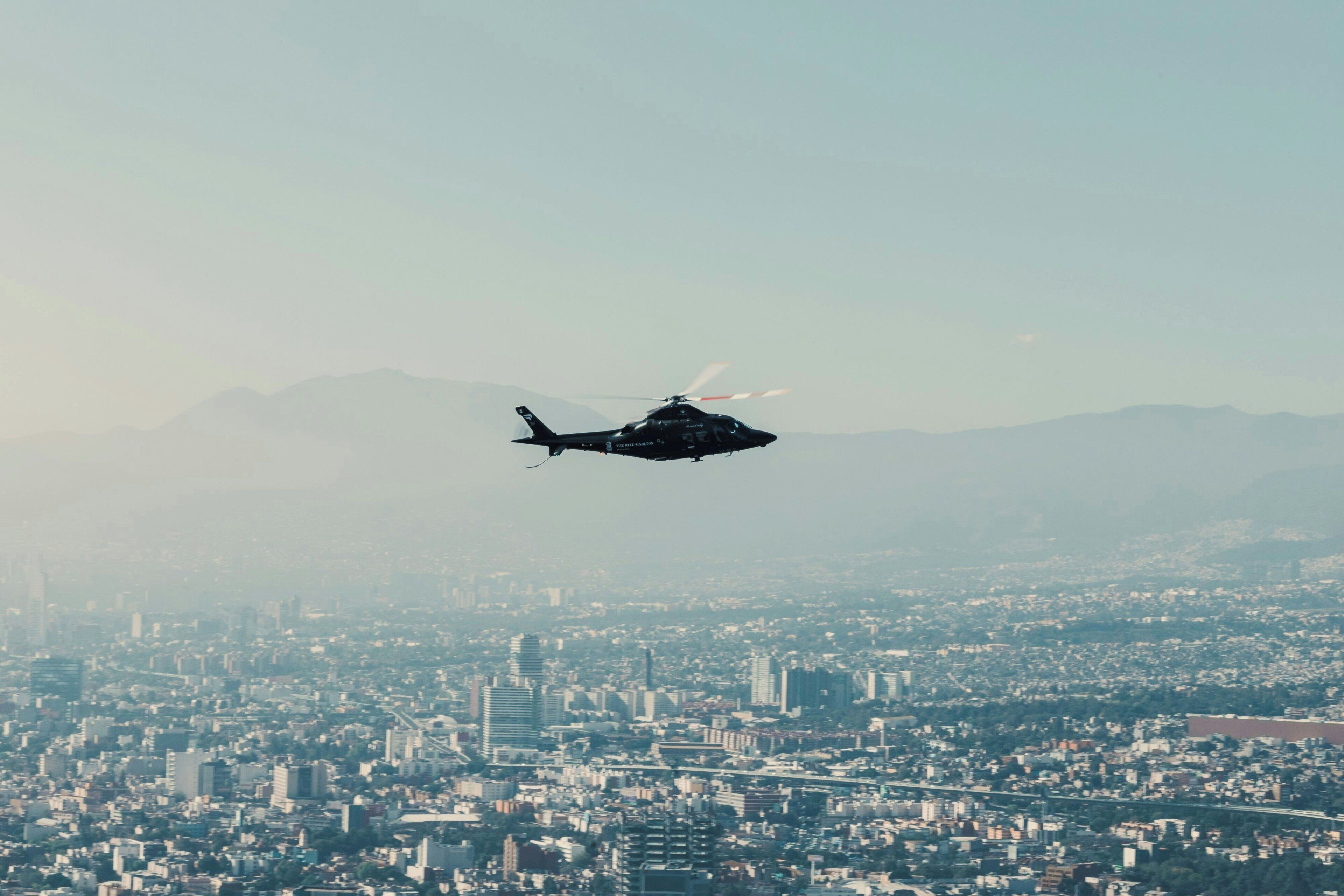 A helicopter flying over a cityscape with mountains in the background.
