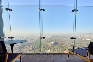A balcony with a glass partition, two chairs, and a table.