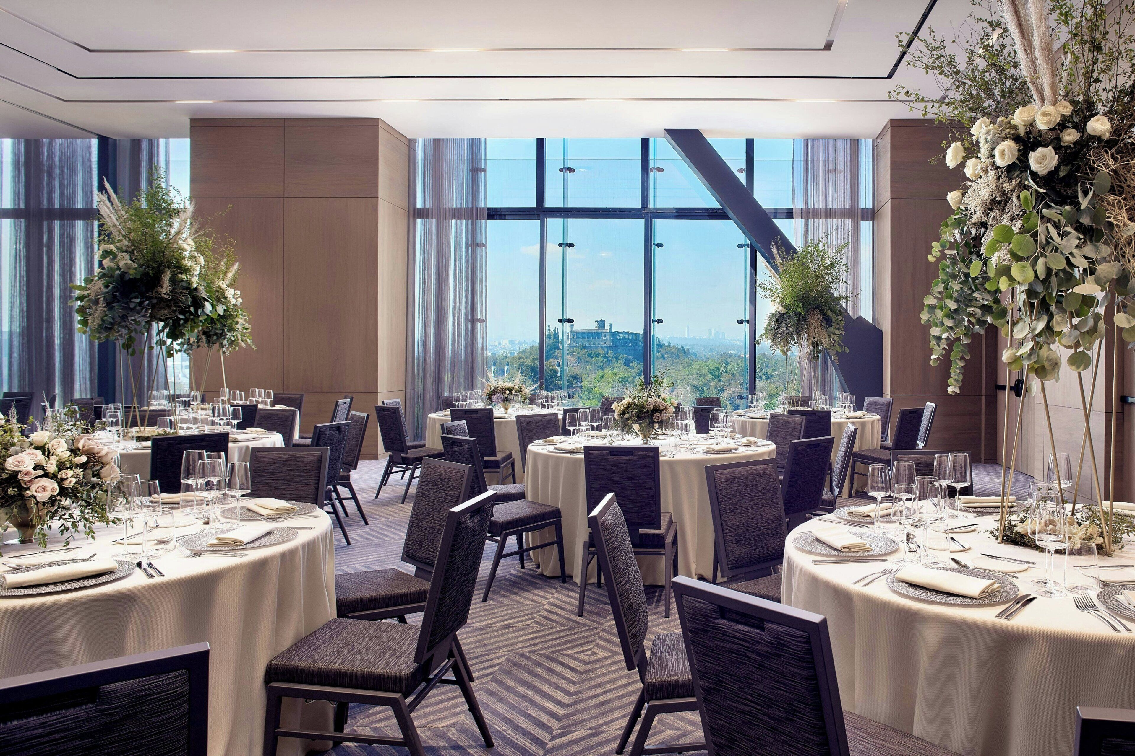 Un espace de restauration d'hôtel avec des tables rondes, des chaises et des centres de table floraux.