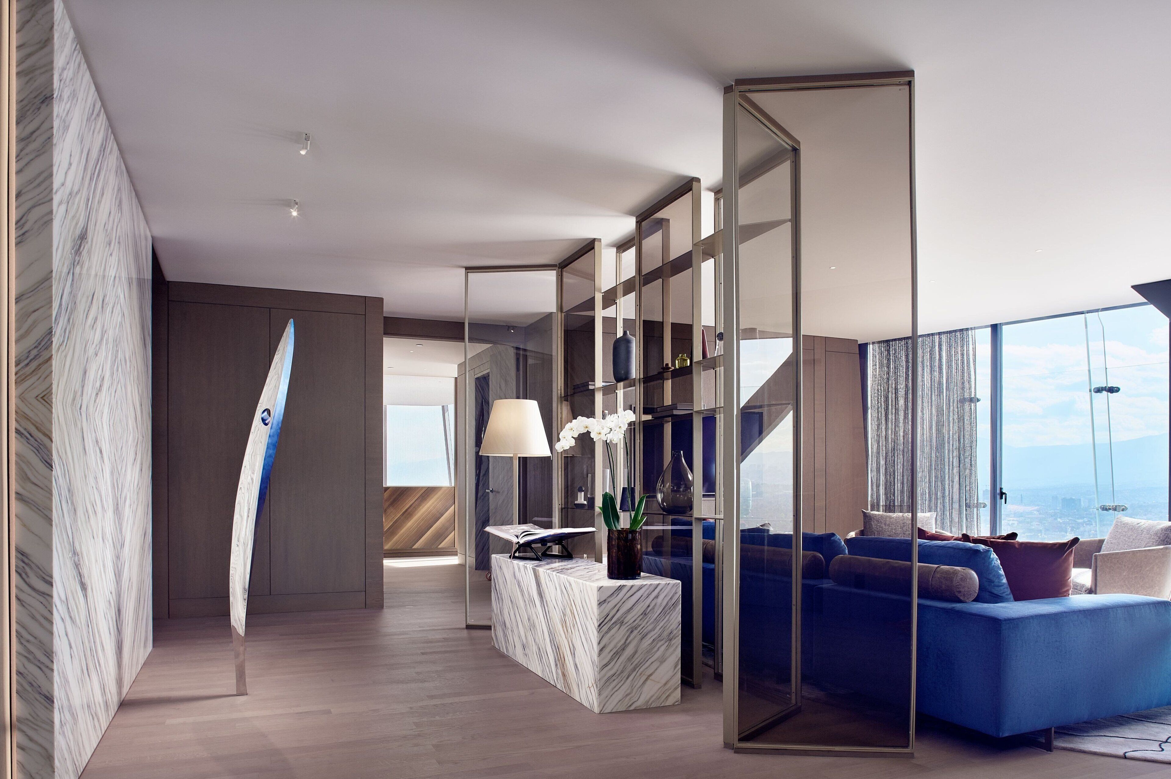 Un salon moderne avec un canapé bleu, une table basse en marbre et une cloison en verre.