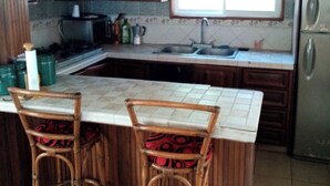 A kitchen with wooden cabinets, a stainless steel refrigerator, a double sink, and two bar stools with patterned cushions. - Beach house (Cumayasa)