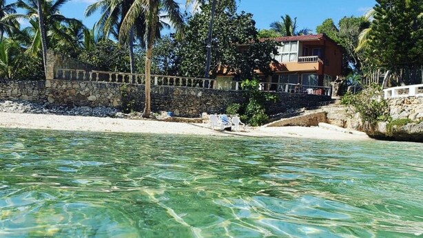 A clear tropical beach with a stone wall and a two-story building in the background. - Beach House ( Hidden Paradise  (Cumayasa)