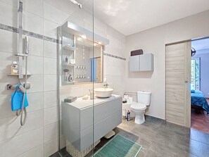 A modern bathroom with a glass shower enclosure, a large mirror, a white sink, and a toilet. - Creole charm with modern comforts (Sainte-Anne)