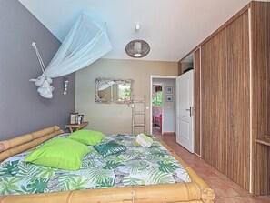 A bedroom with a bed, a wooden wardrobe, a mirror, and a ceiling fan. - Creole charm with modern comforts (Sainte-Anne)