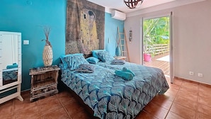 A bedroom with a bed, a large painting, a ladder, and a view of the outdoors. - Creole charm with modern comforts (Sainte-Anne)