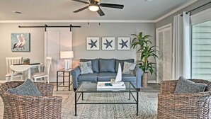 A living room with a gray sofa, wicker chairs, a glass coffee table, a ceiling fan, and wall art. - Couple’s Retreat w/ Balcony in Surfside Beach! (Surfside Beach)