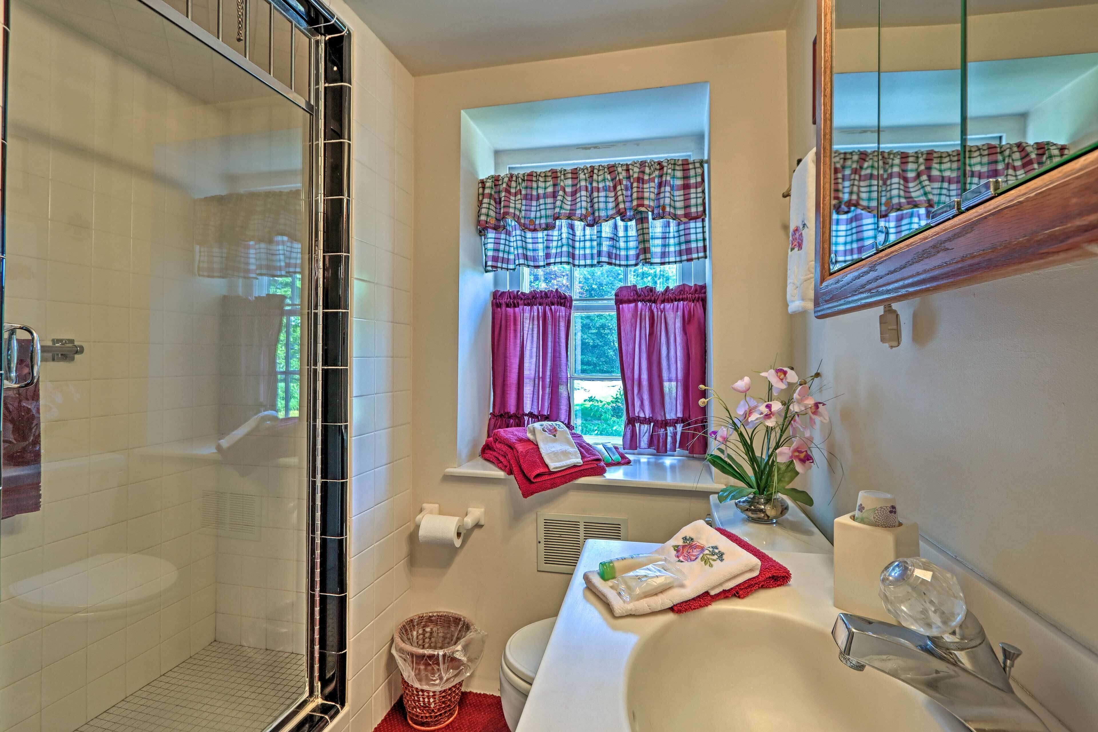A bathroom with a shower, toilet, sink, and window with curtains.