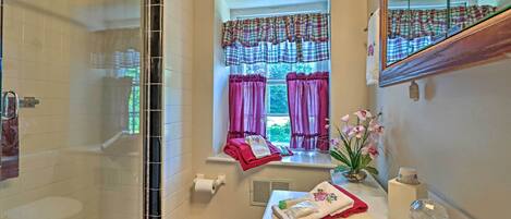 A bathroom with a shower, toilet, sink, and window with curtains.