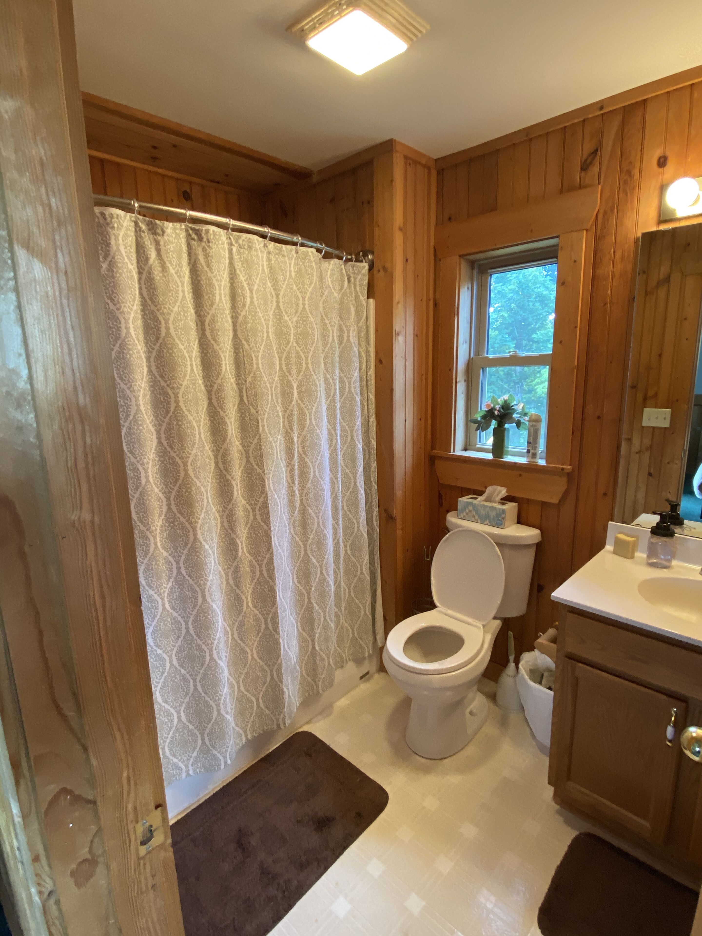 A wooden-paneled bathroom with a toilet, sink, and window.