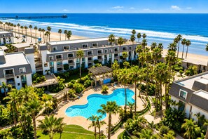 A resort with a central swimming pool, beachfront views, and a pier in the background.