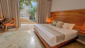 A hotel room with a large bed, a wooden headboard, a nightstand with a lamp, a chair, and a view of a garden through the window.