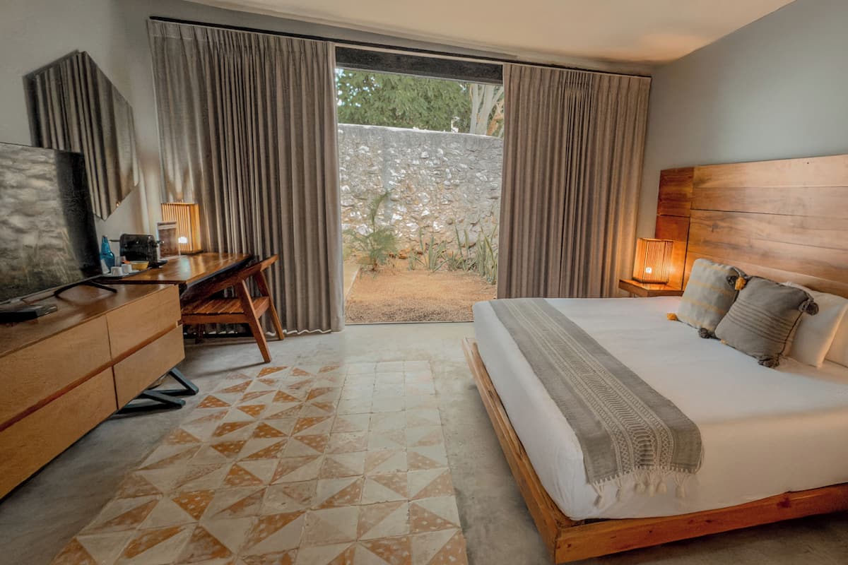 A hotel room with a bed, a desk, a chair, a TV, and a view through the curtains.
