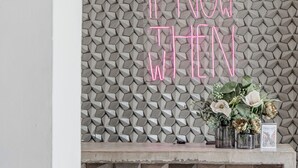 Un intérieur moderne avec un mur orné d'un motif géométrique, un panneau lumineux au néon et un vase décoratif rempli de fleurs.