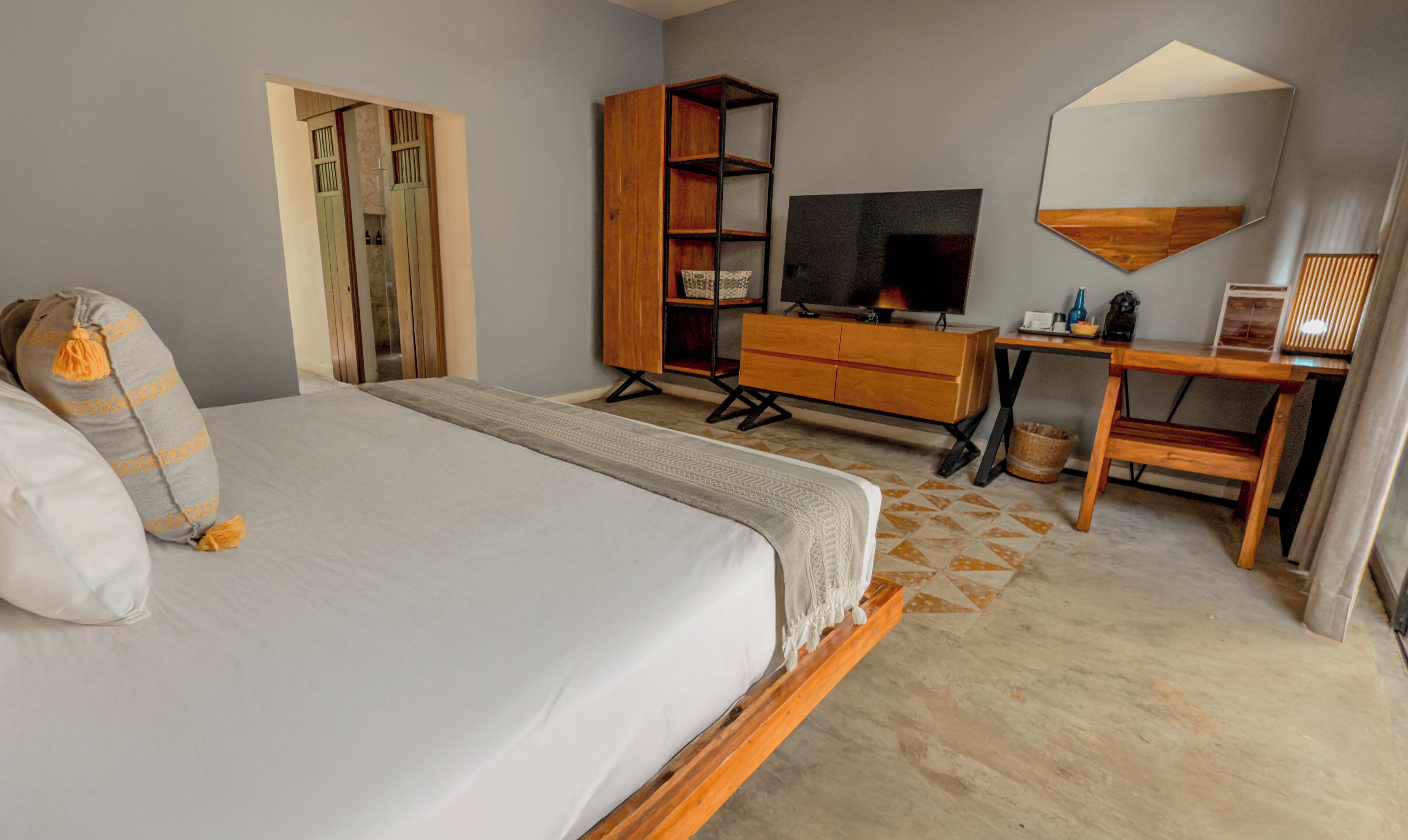A bedroom with a bed, a wooden wardrobe, a TV, a desk, and a mirror.