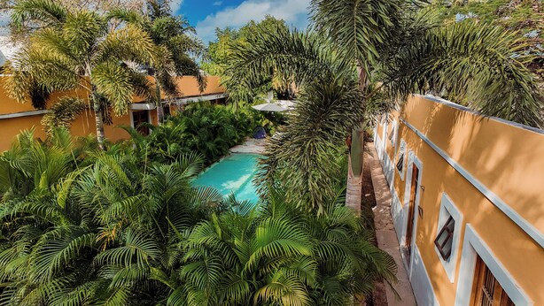 A pool surrounded by lush greenery and a yellow building with white trim.