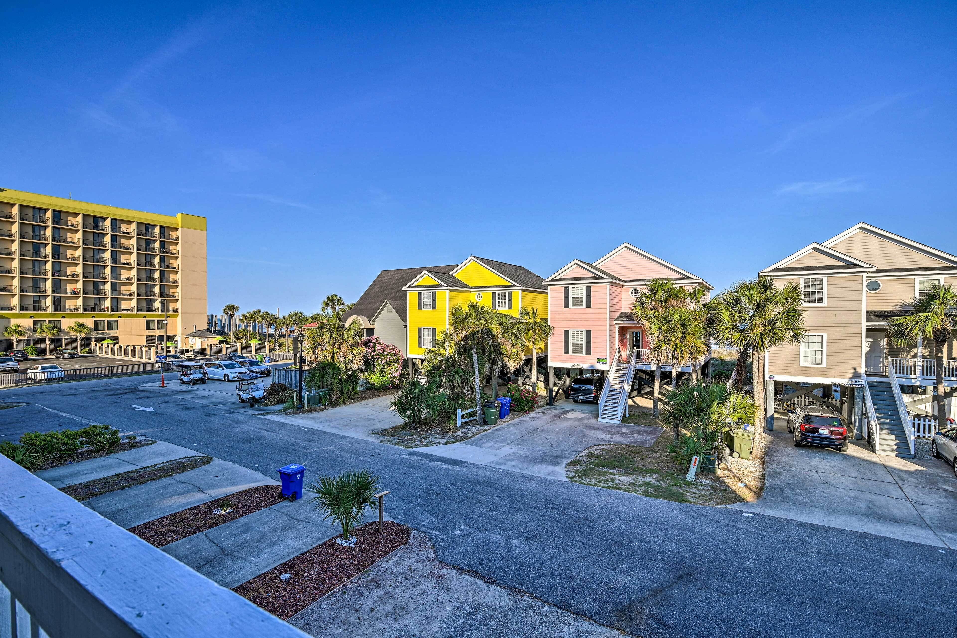 A residential street with colorful houses, a parking lot, and a hotel building.