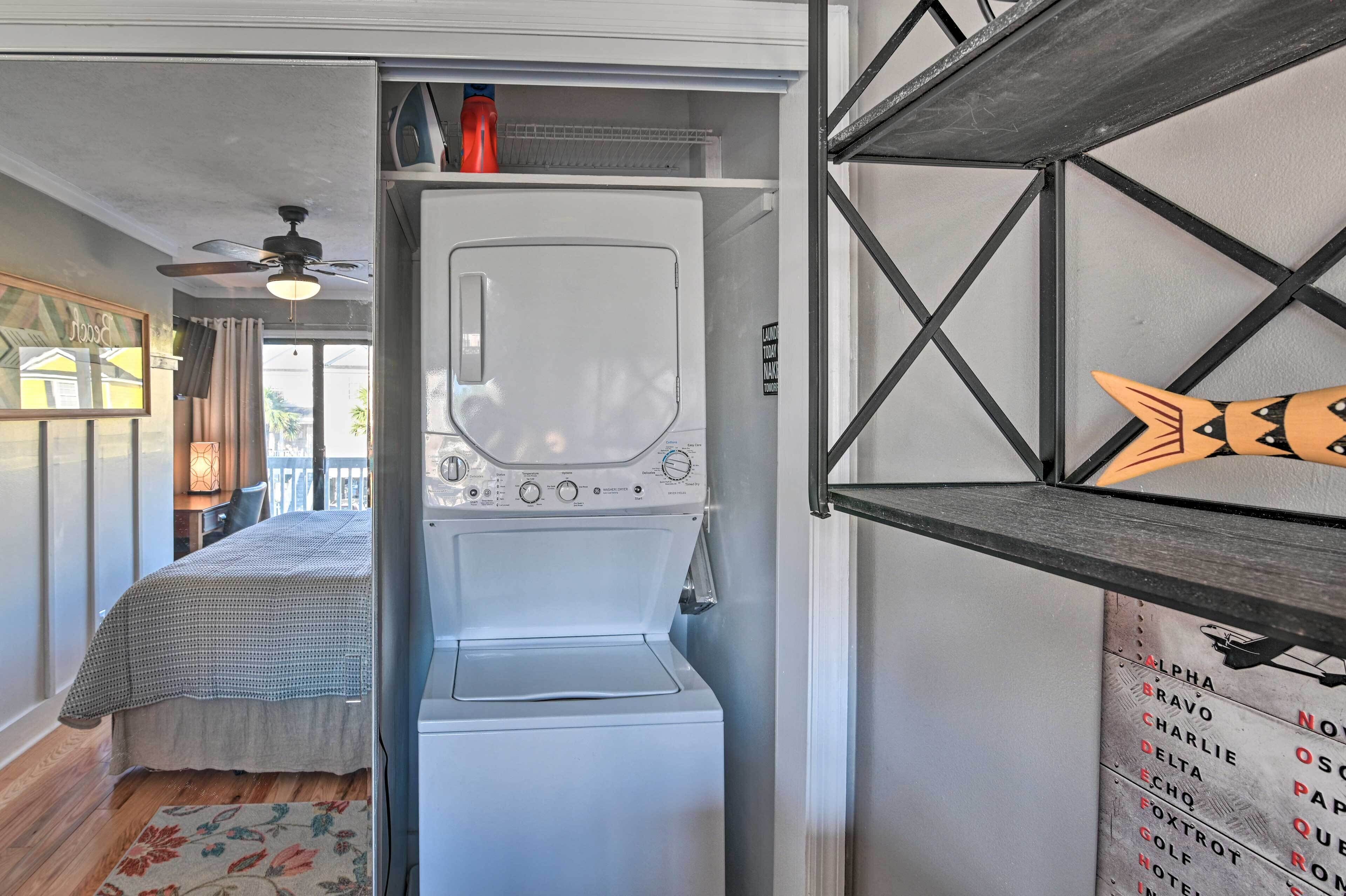 A compact hotel room with a bed, a washing machine, and a small shelf with decorative items.