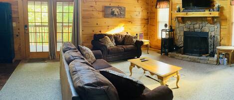 Interior acollidor d'una cabana de fusta amb un sofà, una taula de centre, una llar de foc i una televisió.
