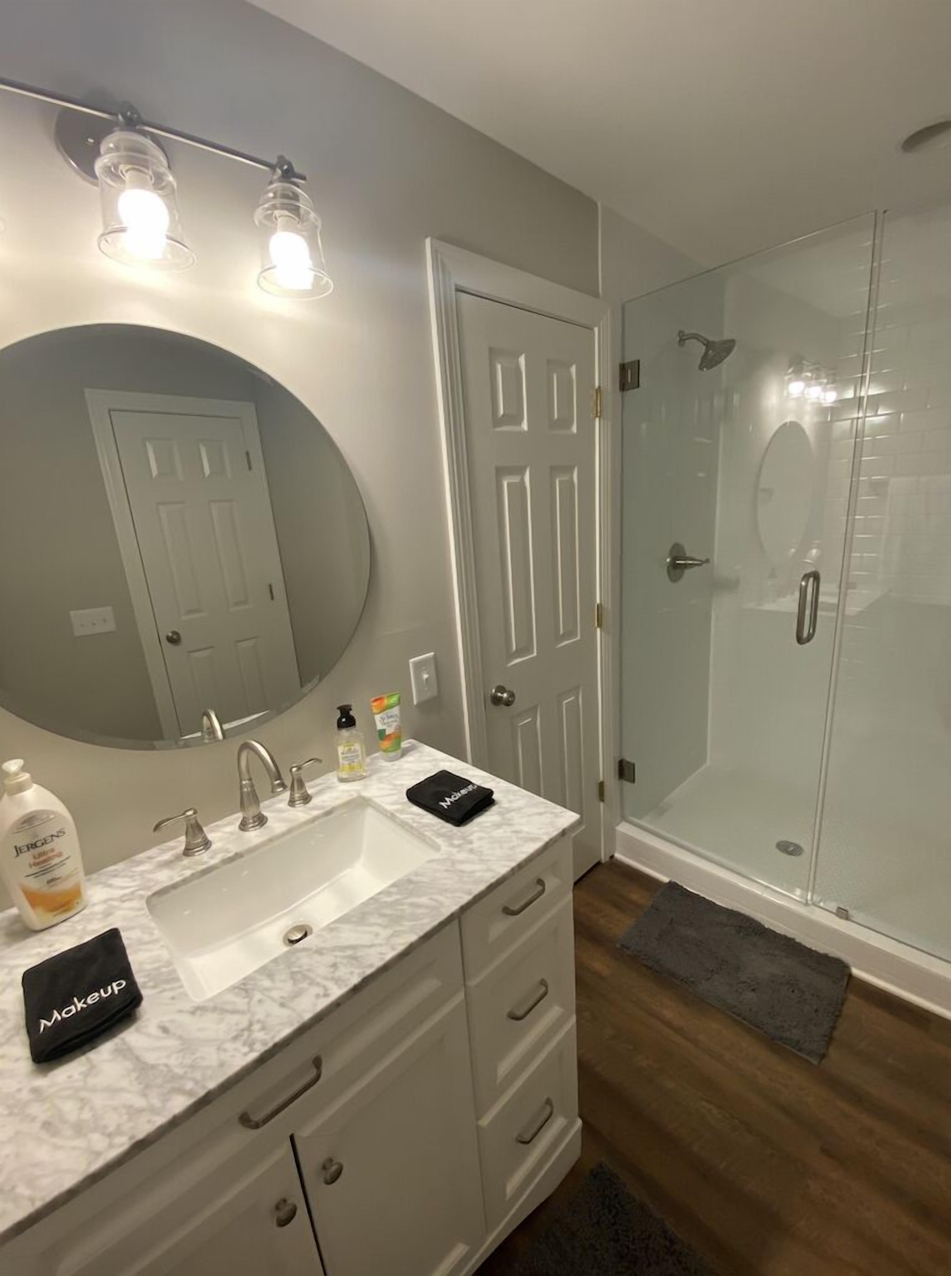 Une salle de bain moderne avec un lavabo en marbre, un grand miroir, une cabine de douche en verre et une douche à l’italienne.