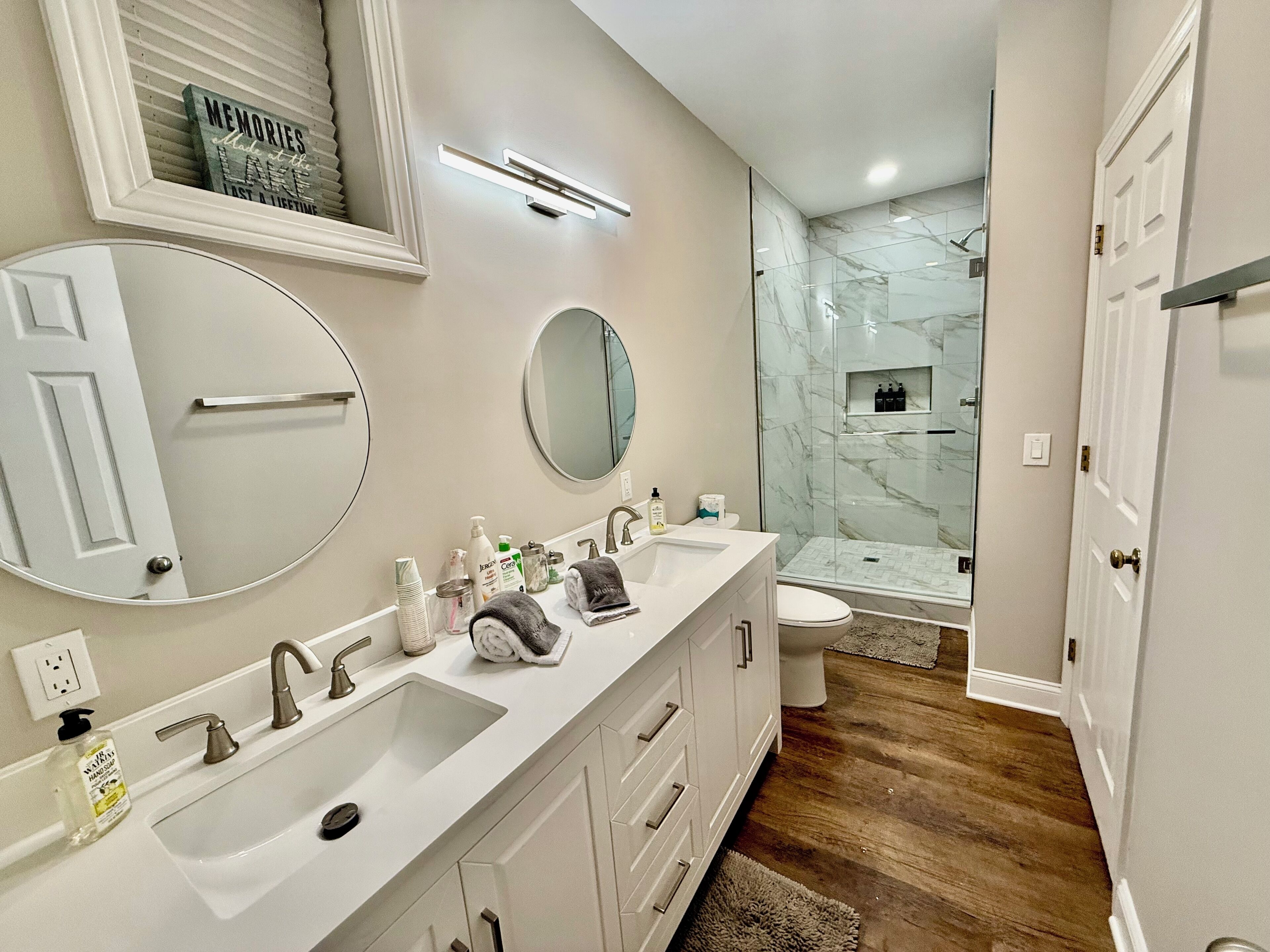 A modern bathroom with two sinks, a large mirror, and a glass shower enclosure.